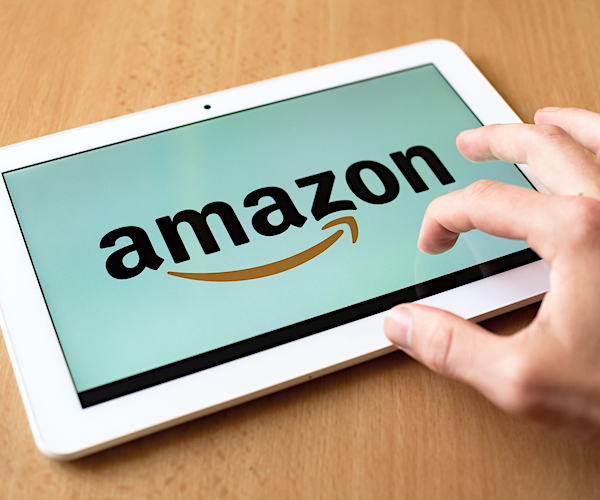 a tablet has the amazon logo on it as a man touches the screen as it lays on a brown table