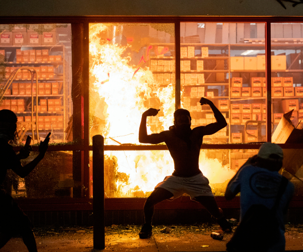 a man poses in front of a business that has been set on fire