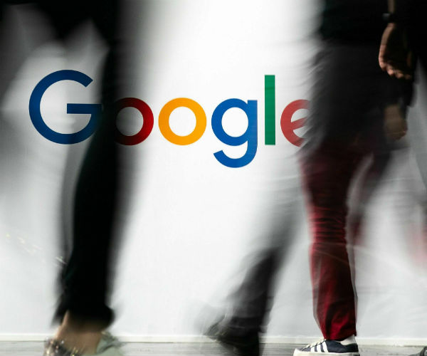 people walking past a google sign on the street