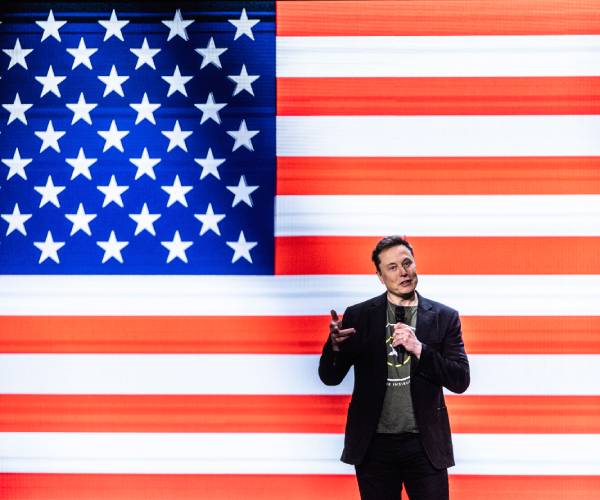 elon musk speaking in front of a giant american flag