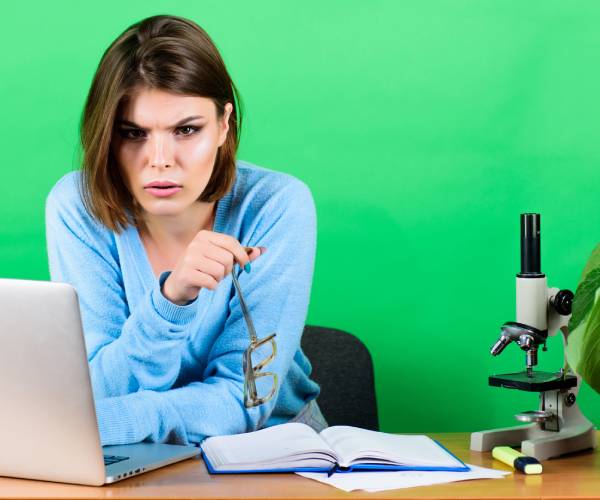 woman writing on laptop with a miscroscope on her desk