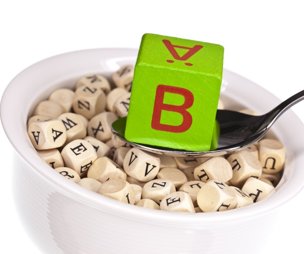 wood dice with different letters in a bowl, and the letter B on dice that is on a spoon above bowl