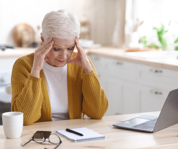 woman at desk, holding her head with headache