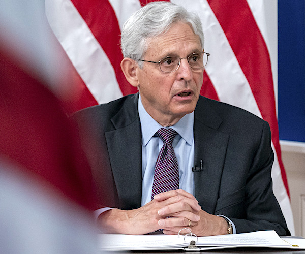 merrick garland sits hands folded on a table of documents