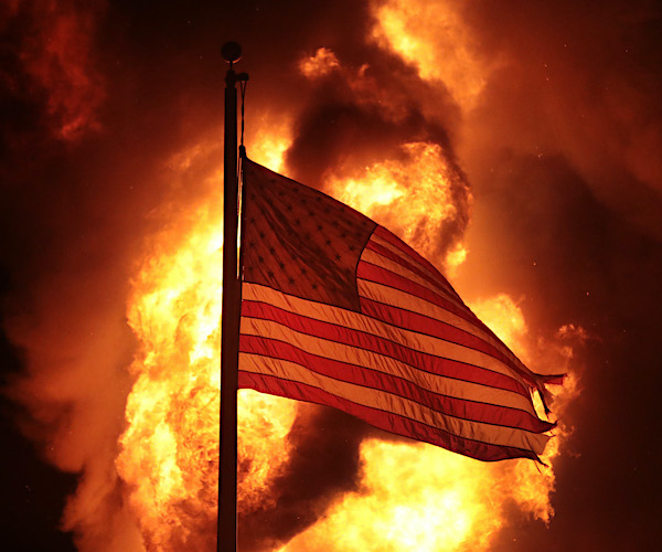 a black lives matter inferno is burning at night behind an american flag waving in the smoke and wind