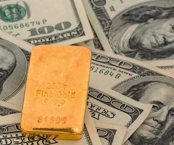 a small gold bar lying on hundred dollar bills