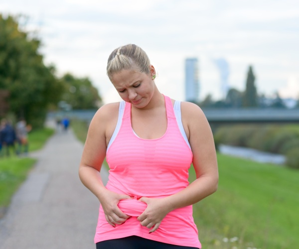 woman in park in athletic wear, pinching some fat on waist