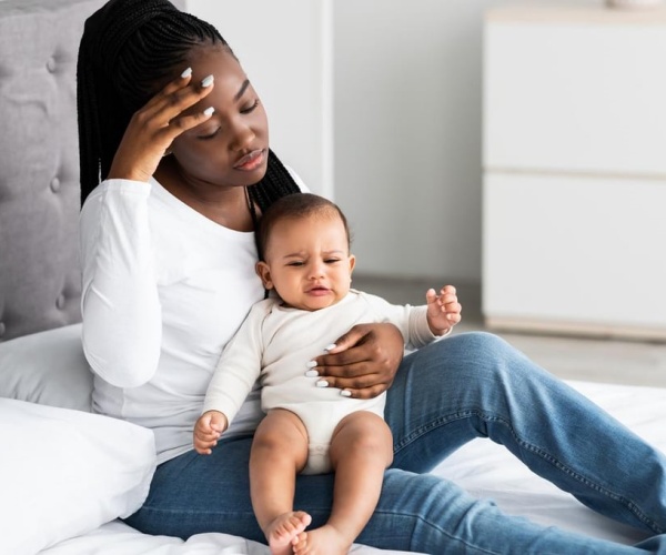 Woman looking sad and distracted sitting on bed with baby