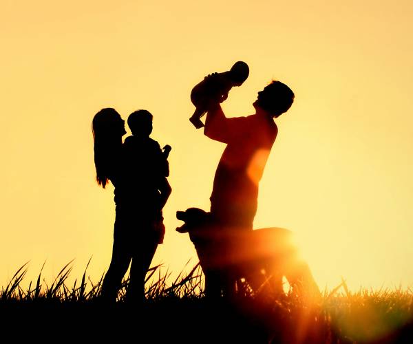 a mother, father and two children playing against a sunset