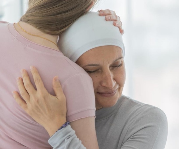 woman undergoing breast cancer treatment with scarf on head hugging another woman