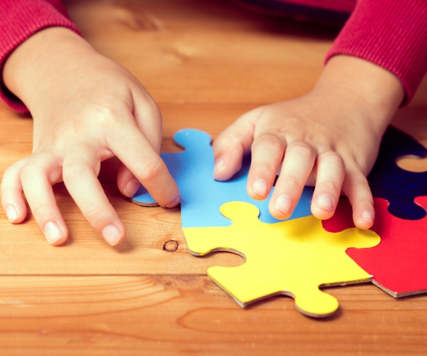 hands of a child putting together puzzle pieces, signifying autism