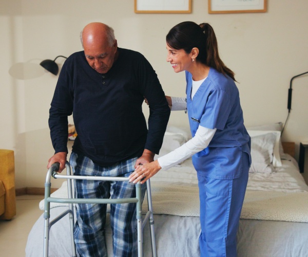 physical therapist getting man out of bed to walk with walker