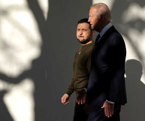 biden and zelensky walking side by side in profile with the shadow of a tree on the wall behind them