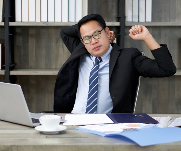 man sitting at desk at work, stretching a little after sitting a long time