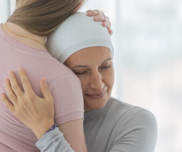 woman with hair loss from chemo wearing a cotton hat hugging a friend