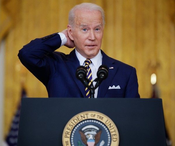 joe biden standing behind the presidential podium with his hand behind his neck.