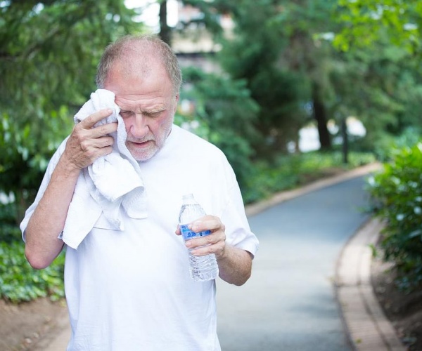 older man walking outside with water bottle, wiping sweat with towel