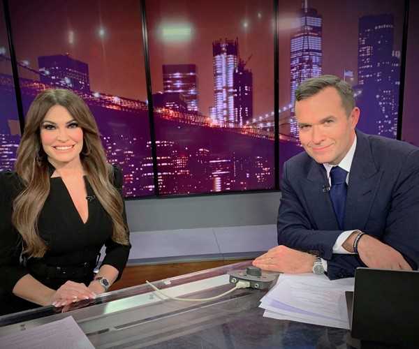 Kimberly Guilfoyle and Newsmax host Greg Kelly smile on set