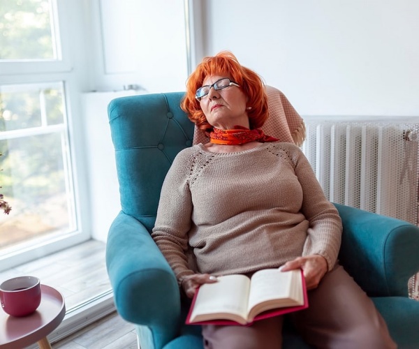 older woman asleep during day on chair while reading book