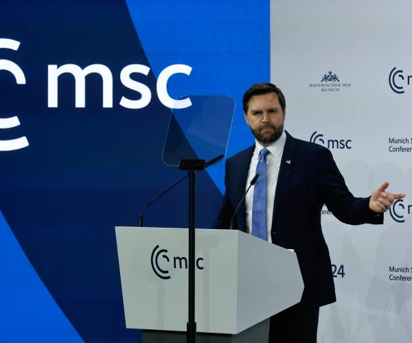 vance gestures with his hand as he stands behind a podium with the munich conference logo