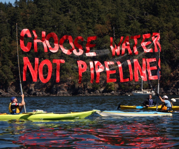 people hold up a banner saying "choose water not pipelines" while kayaking