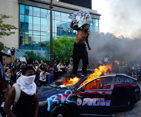 protestor stands on burning police car