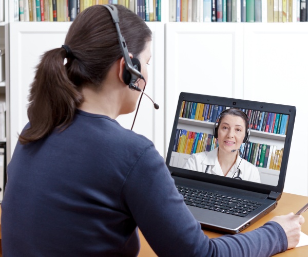 woman with headset talking to her doctor on her computer for a telehealth appointment