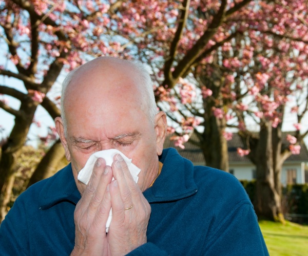 man standing in front of cherry tree blowing his nose