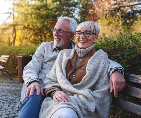 older couple, smiling, sitting on a bench in park together