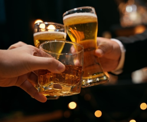 3 people doing a 'cheers' at night at a bar or party with three different drinks