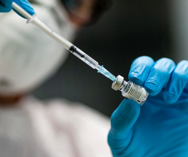 health worker puts a syringe in a glass container of covid vaccine