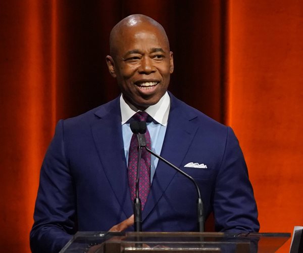 eric adams smiles at a podium