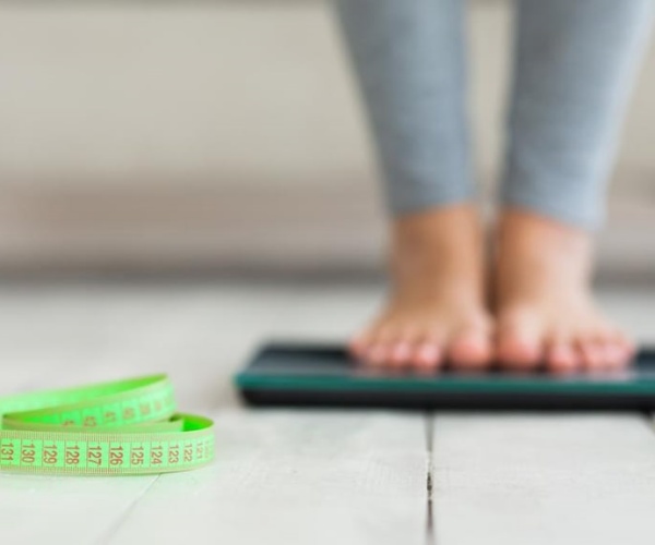 woman's feet on scale, with measuring tape next to it on floor