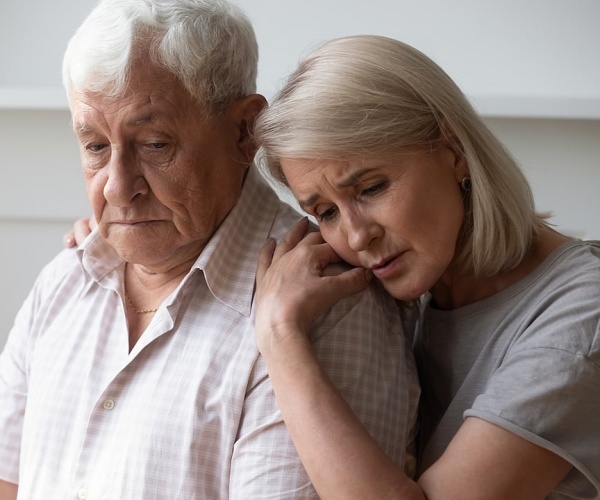 woman hugging older man, both looking sad
