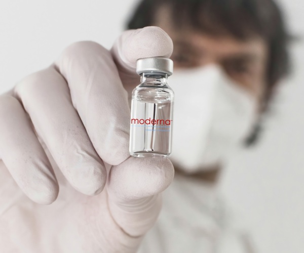 healthcare worker holding up a vial of vaccine with Moderna logo