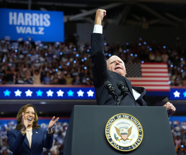 tim walz raises his fist at the lectern with kamala harris behind him