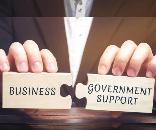 a businessmans hands holding puzzle pieces labeled business and government support