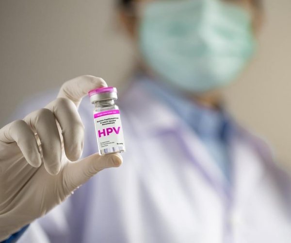 healthcare worker holding up a vial with a label that says 'HPV'