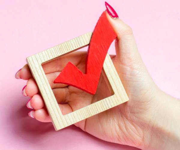 a womans hand holding a wooden cutout of a checkmark in a box