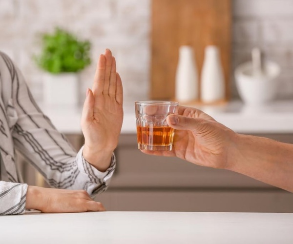 woman holding up hand to say 'no' to a glass of liquor being offered