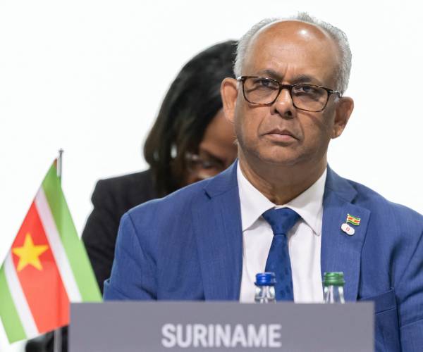 albert ramchand ramdin behind a plaque that reads suriname next to a suriname flag