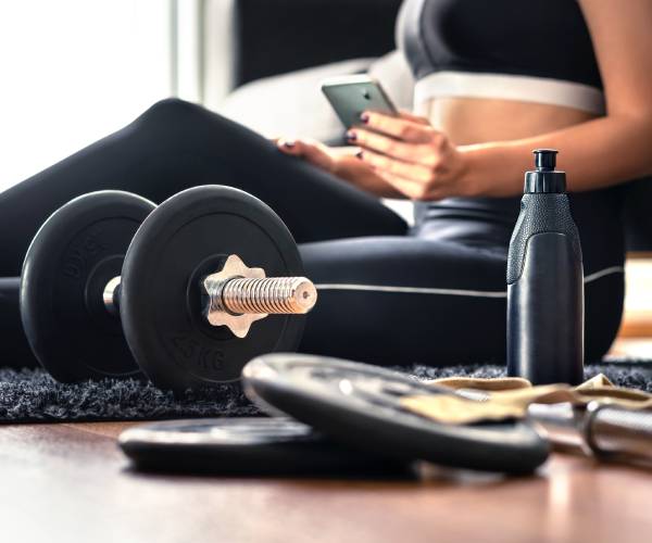 a woman checks her phone with workout equipment in the foreground