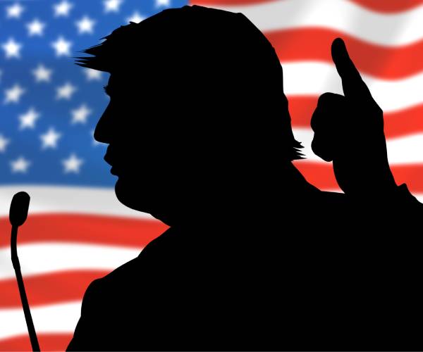 silhouette of donald trump speaking with an american flag in the background