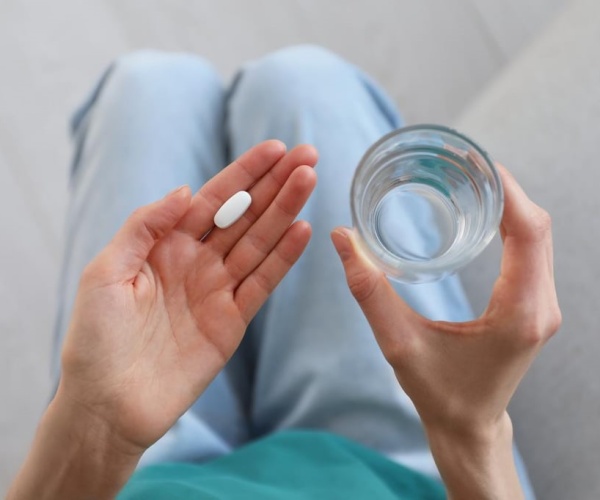 woman sitting, holding a pill and glass of water