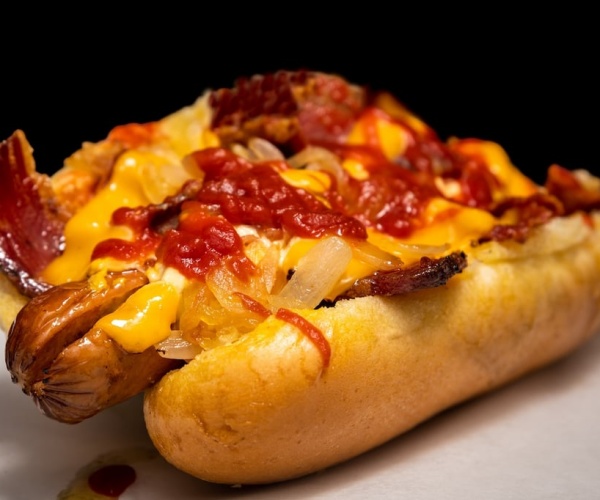 hot dog on a bun with cheese, bacon sauce