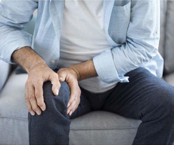 man sitting in armchair holding knee in pain