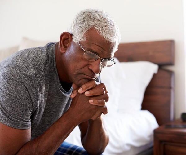 older man sitting on side of bed looking depressed