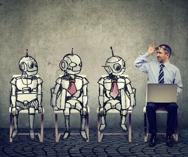 a man sitting with a laptop computer raises his eyeglasses to look at three robots seated next to him