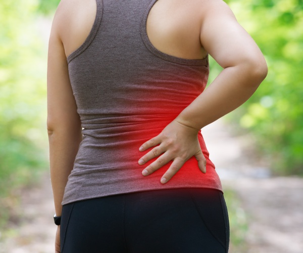 woman walking outside in park with hand on back in pain