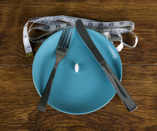 plate with a pill in middle, knife and fork and measuring tape